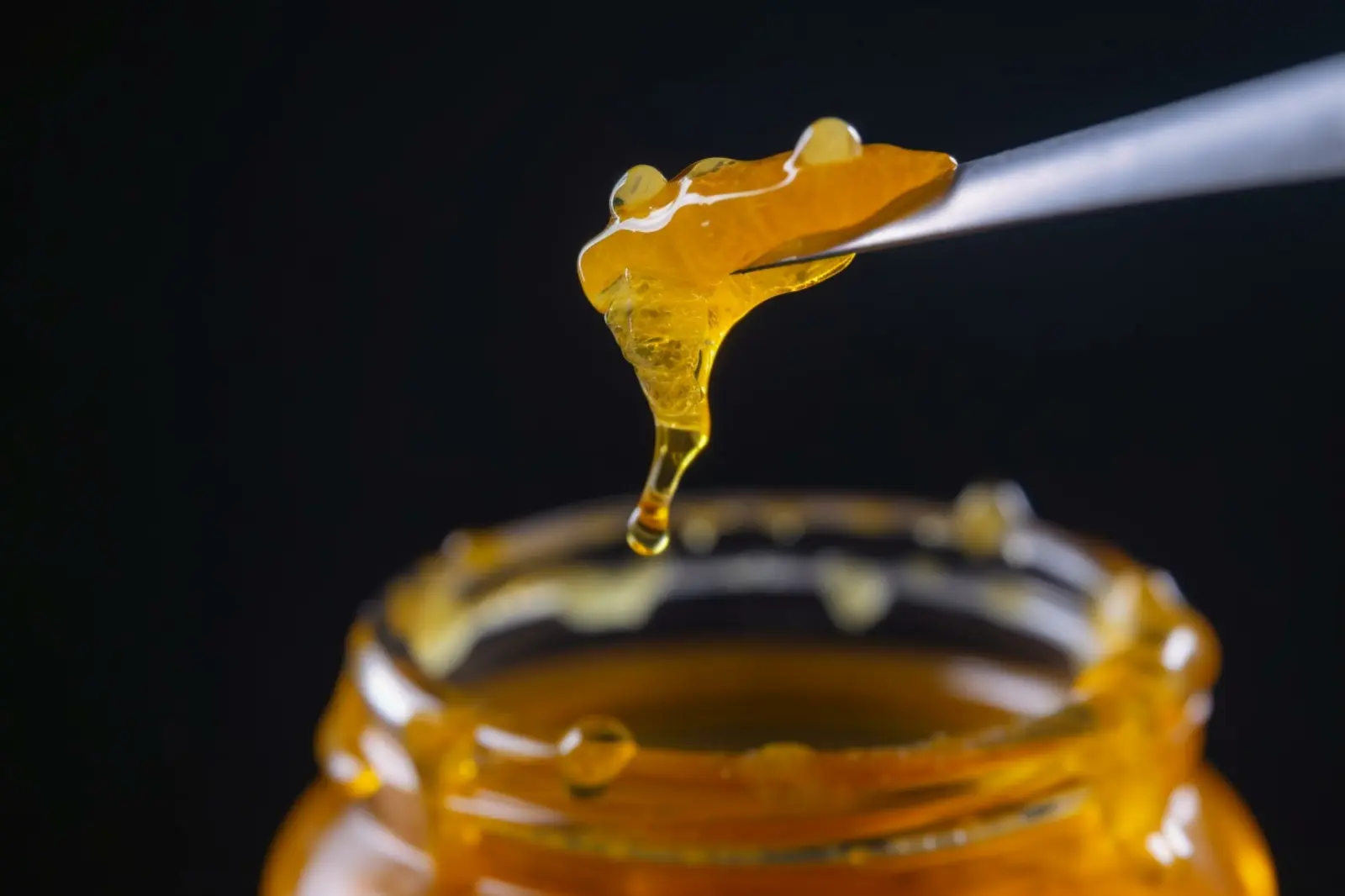 Cannabis concentrate dripping from dab tool over glass jar